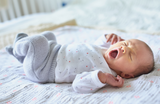 Infant peacefully sleeping in a darkened room, showcasing the importance of REM sleep for brain development, with OtterSpace blackout curtains in the background